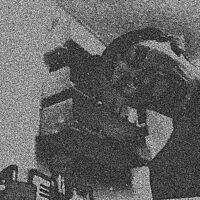 A grainy black and white image showing the distorted face of a young man. In the background there are shelves on the wall above an upright keyboard.